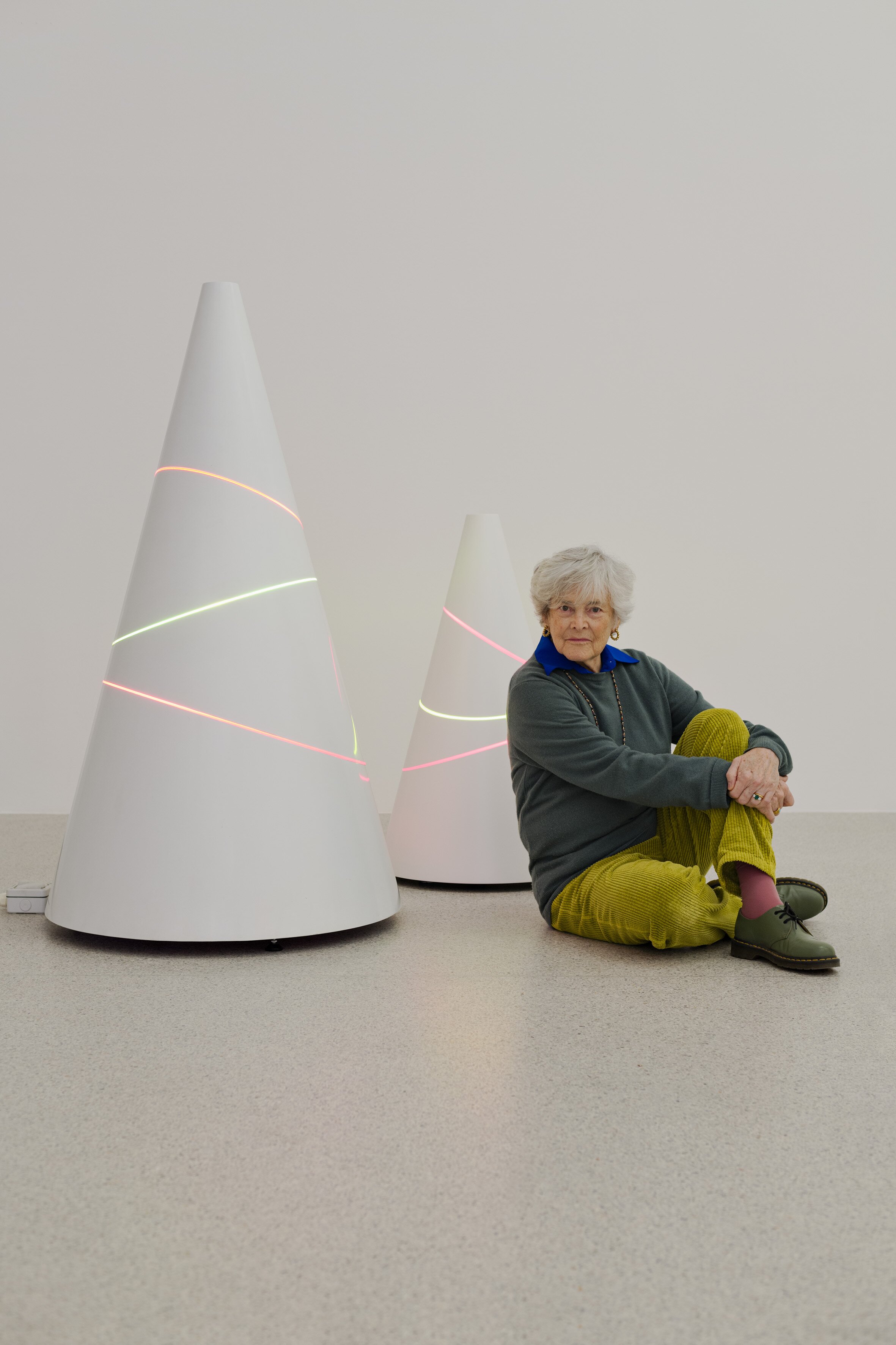 Portrait: Liliane Lijn neben zwei kegelförmigen Kunstwerken