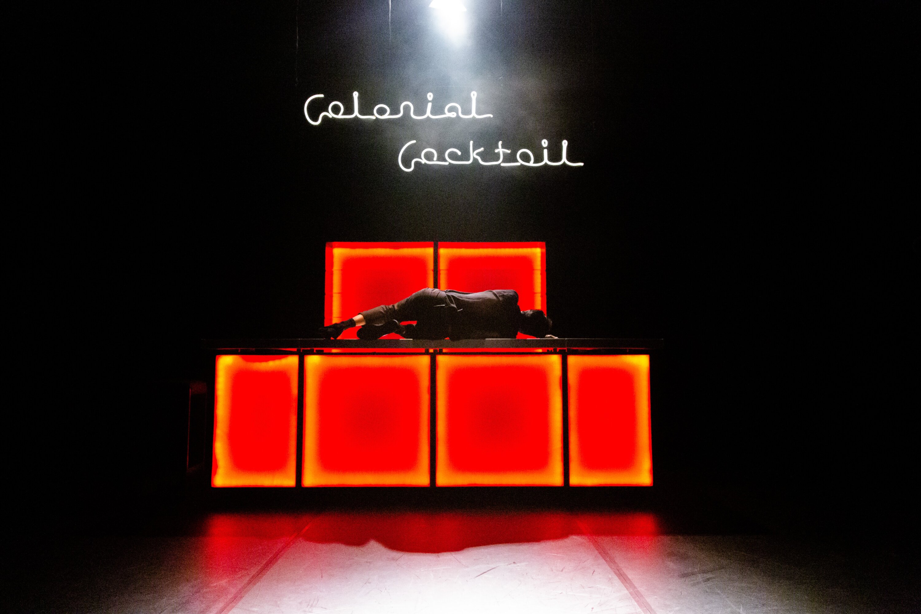 Performanceansicht mit Leuchtschrift Colonial Cocktail und einer Person auf einer Bar liegend