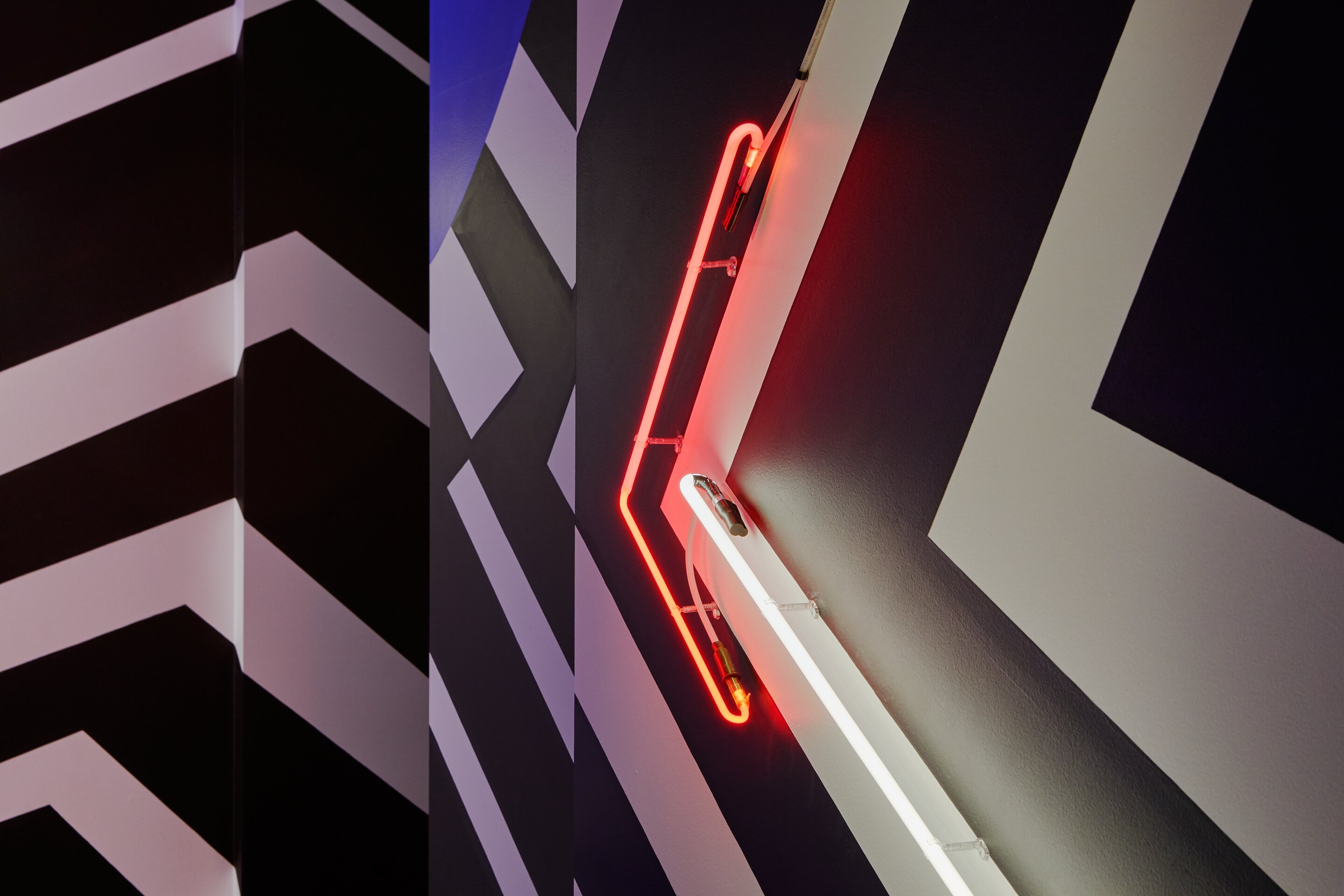 Künstlerische Wandgestaltung mit schwarzweißem Strichmuster und zwei Neonlampen.