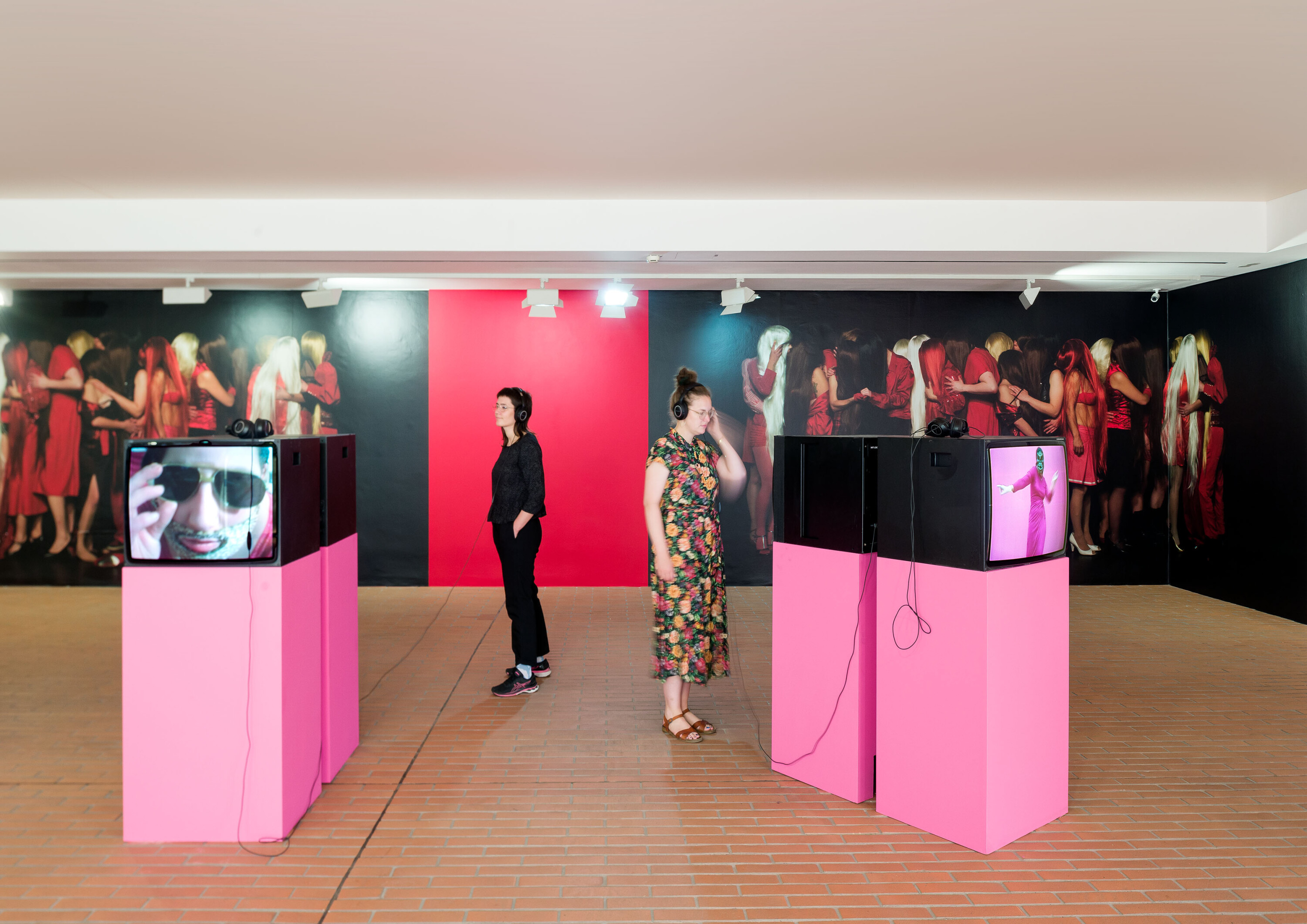 Ausstellungsansicht, Fernseher im Vordergrund, Fototapete mit Menschengruppen im Hintergrund