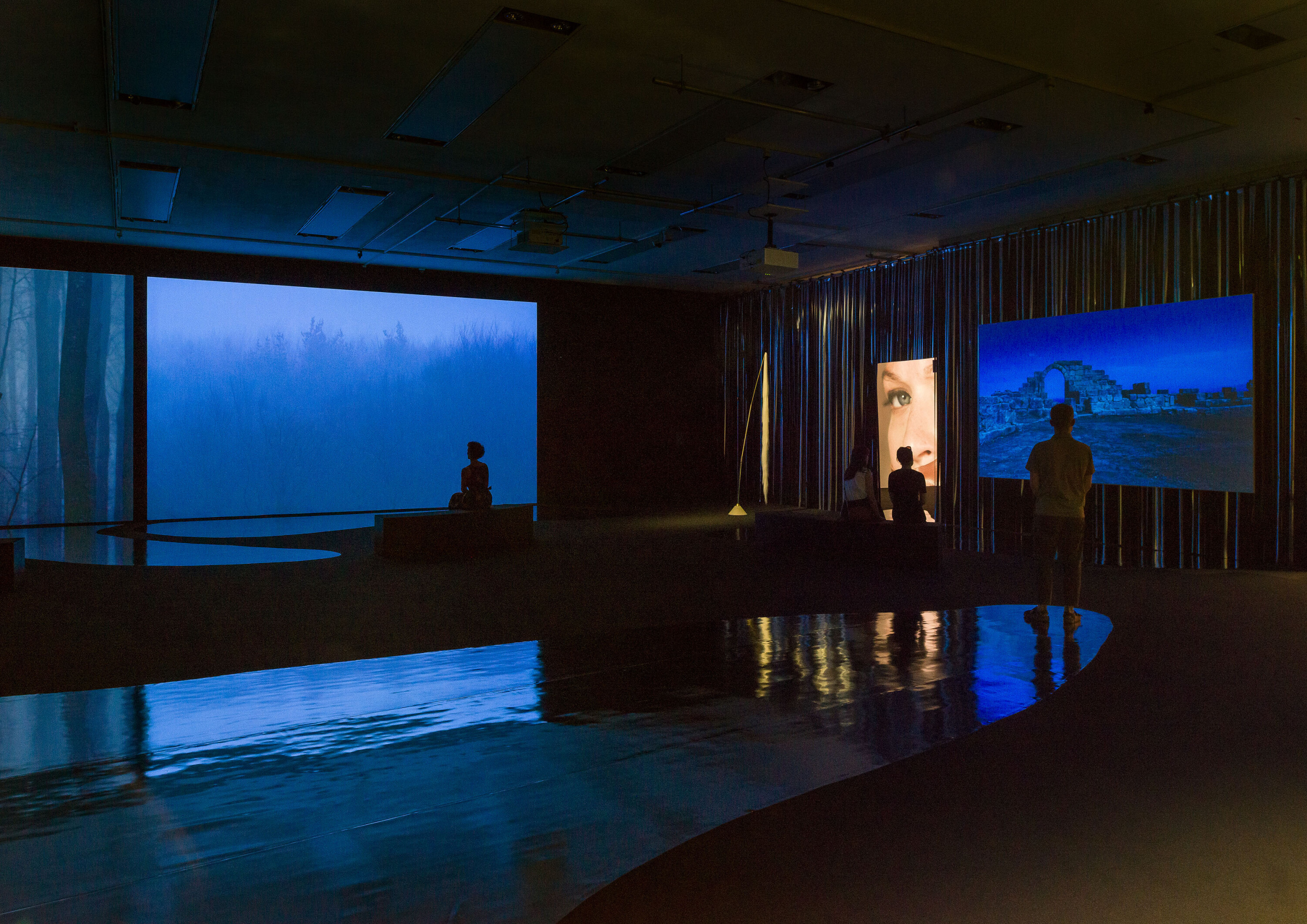 Ausstellungsansicht mit mehreren Filmprojektionen und spiegelndem Boden