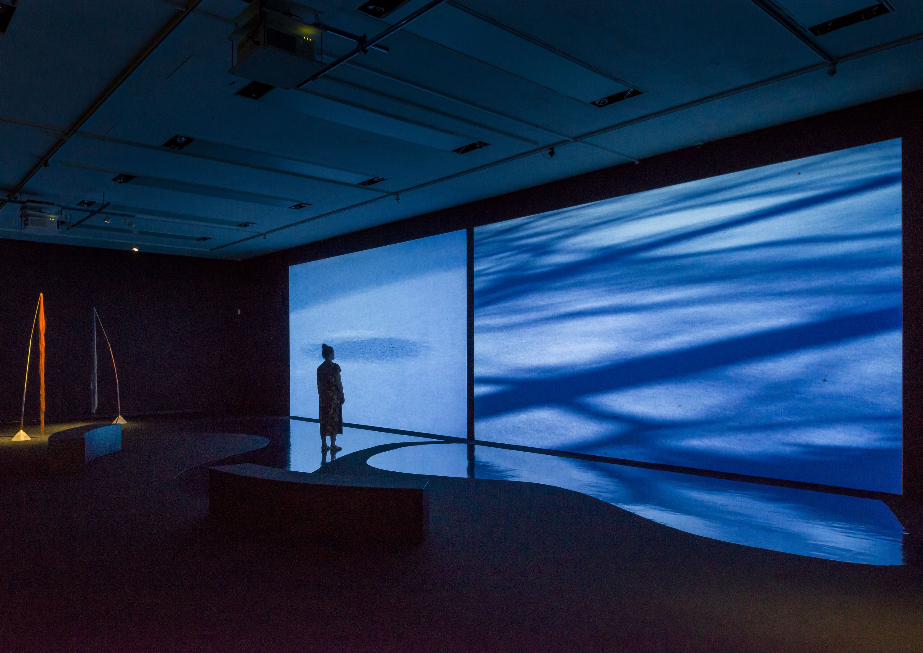 Ausstellungsansicht mit Filmprojektion und Skulpturen am rechten Bildrand