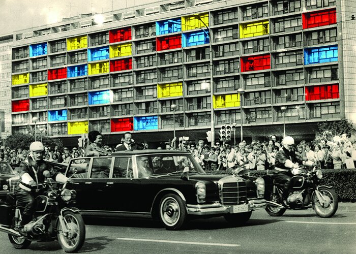 Autoparade mit Polizeibegleitung vor Publikum und Häuserfassade