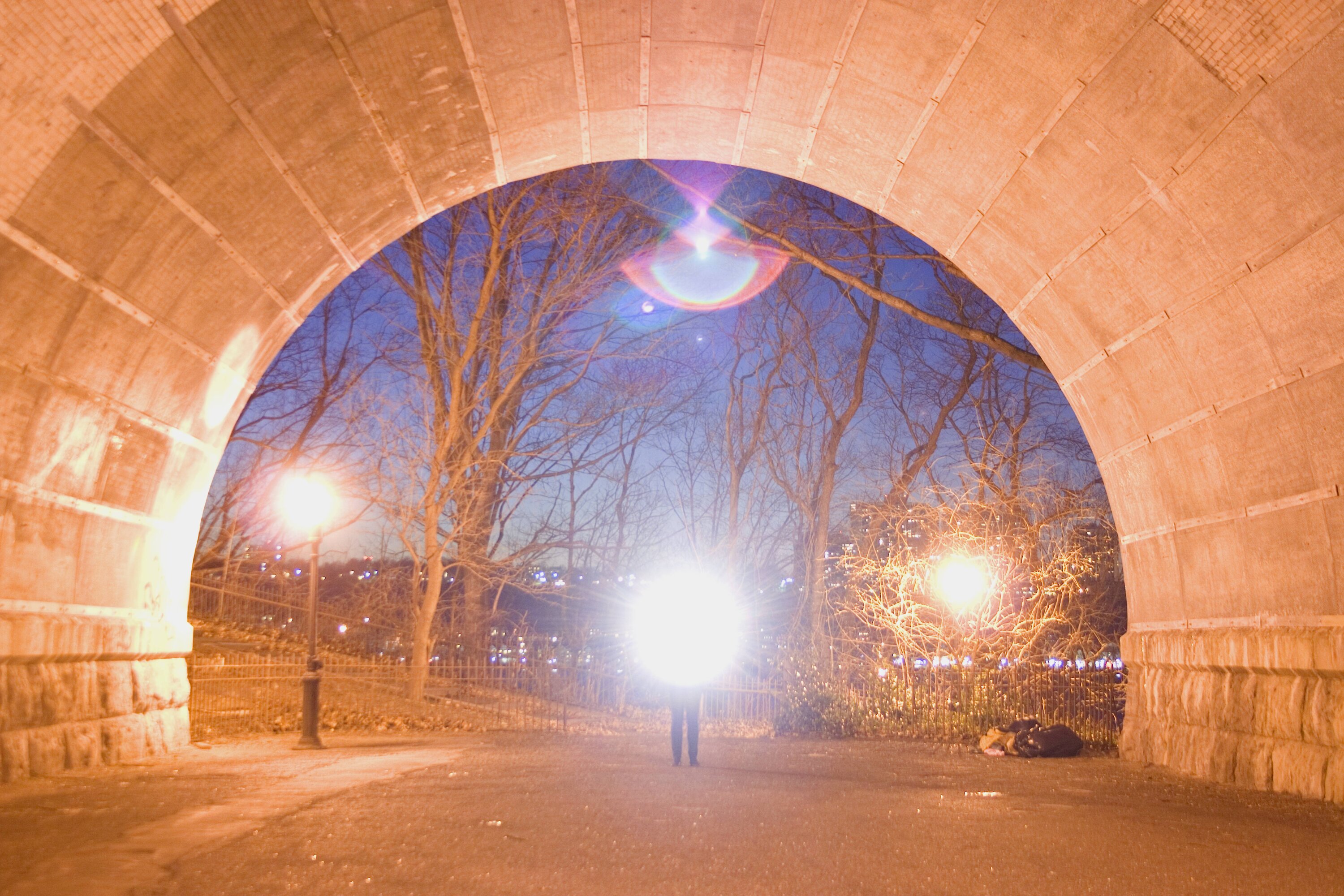 Am Ende eines Tunnels steht eine Person mit Lampe und h&uuml;llt die Umgebung in warmes Licht.