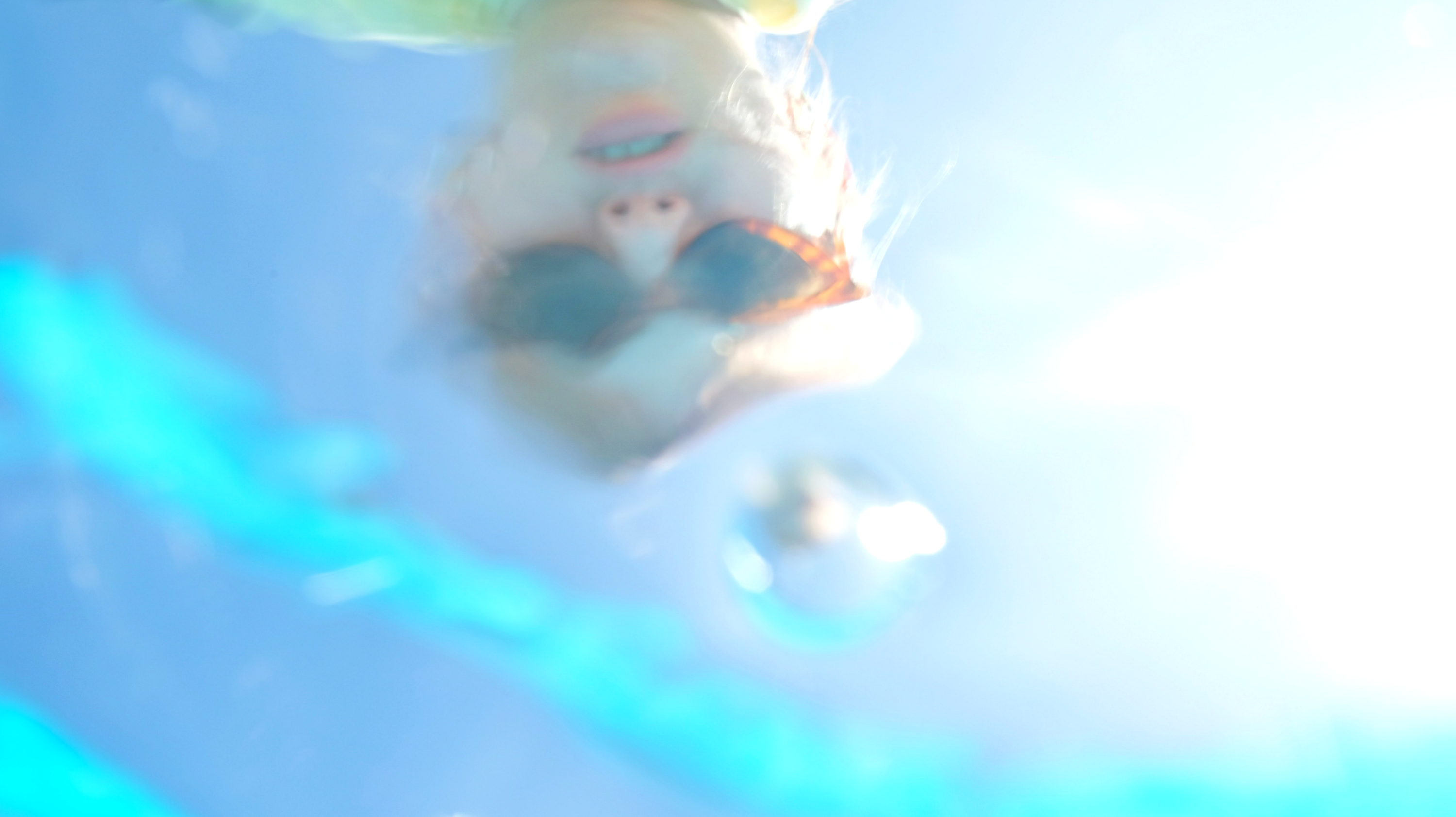 Ein Spiegelbild eines Gesichts mit einer Sonnenbrille in der Wasseroberfläche eines Pools.