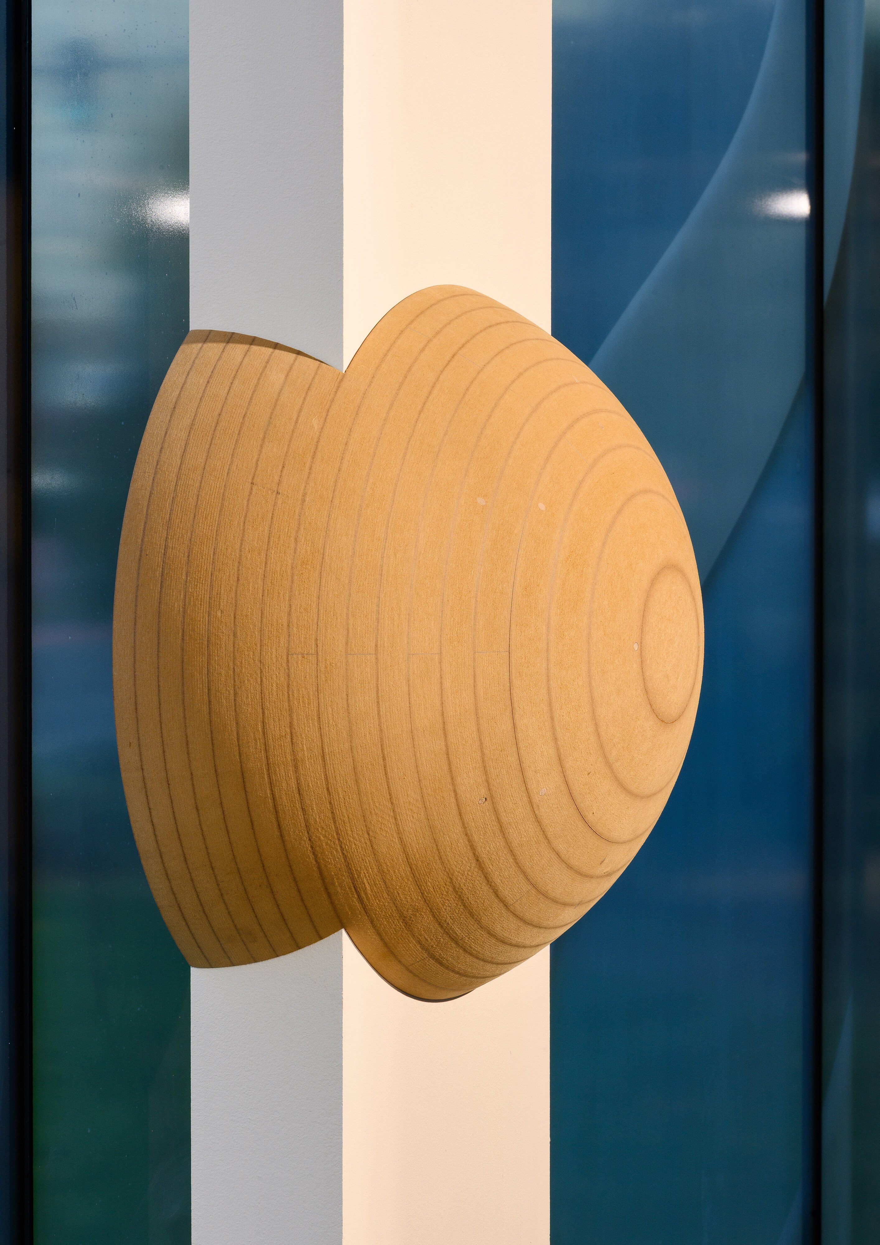 Ausstellungsansicht mit einer hölzernen, kugelförmigen Skulptur, die sich in die Wand einfügt.